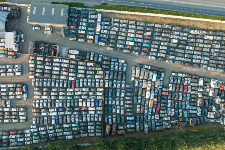 Aerial view of big parking lot of junkyard with rows of discarded broken cars