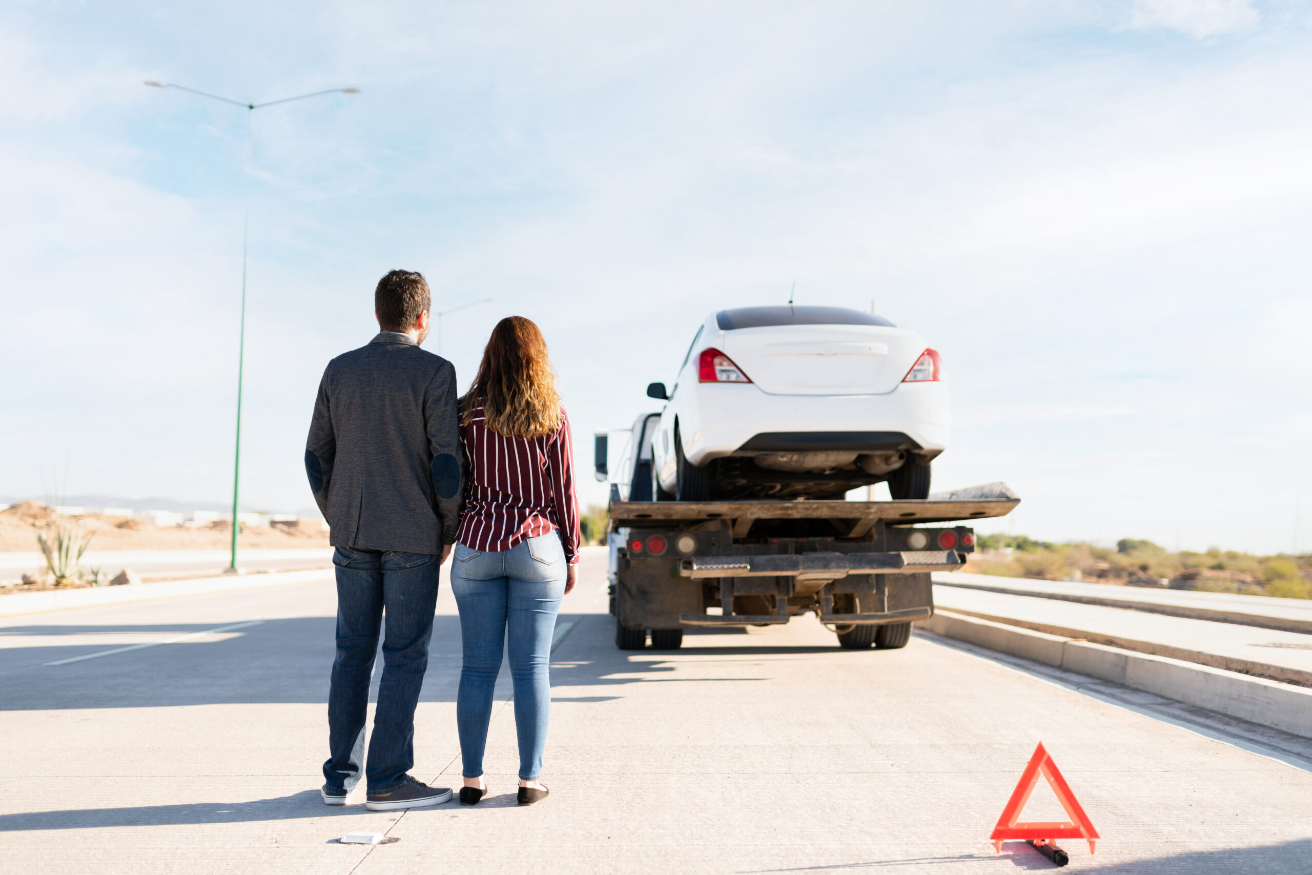 Rear view of a couple watching their car on a tow truck
